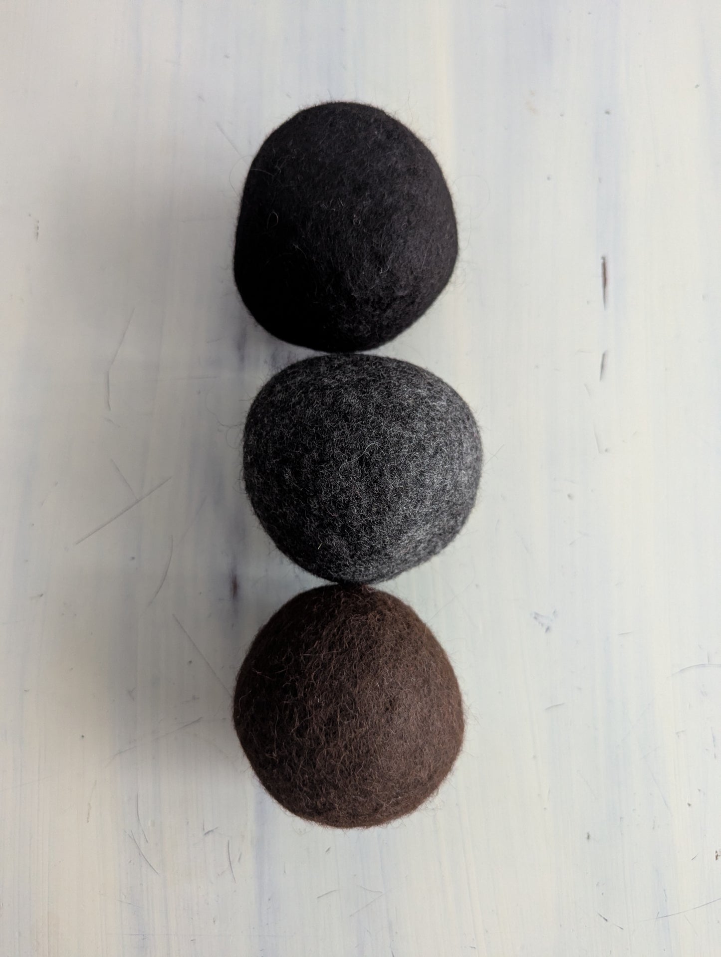 Three felted wool dryer balls in black, gray, and brown on a white background