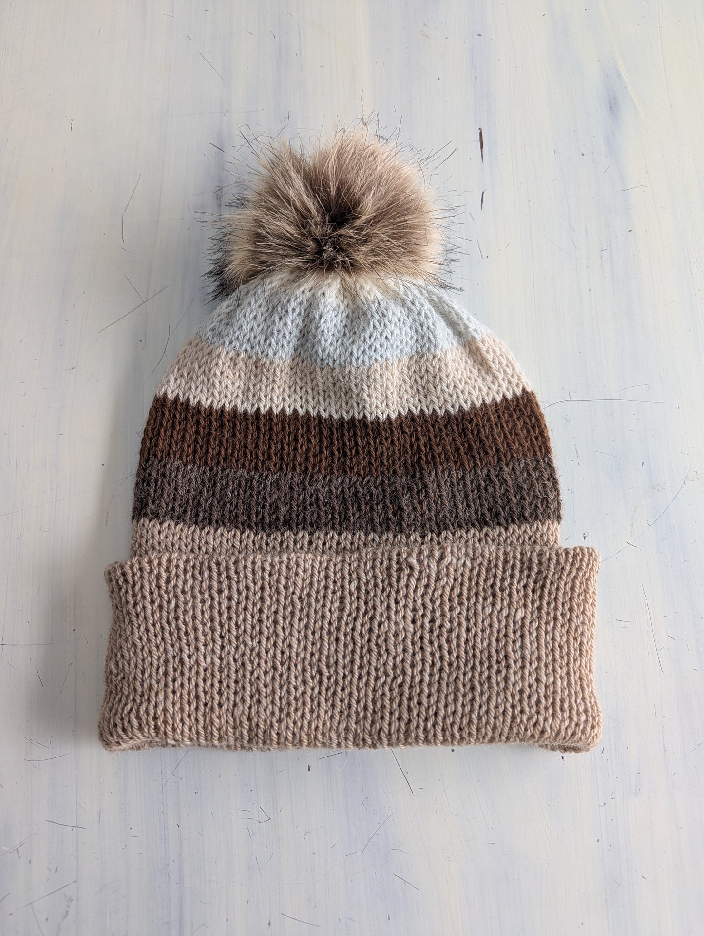 Knitted beanie with striped pattern and pom-pom on a light background