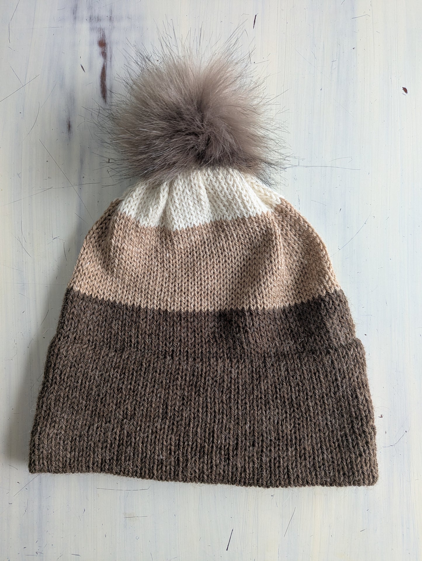 Knitted beanie with a fur pom-pom on a light wooden surface