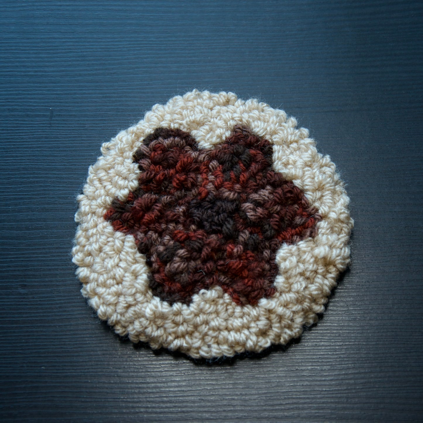 A hand-stitched, circular coaster with a textured red flower in the centre, placed on a dark surface