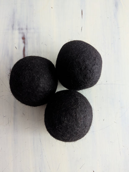 Three black felt dryer balls on a white surface