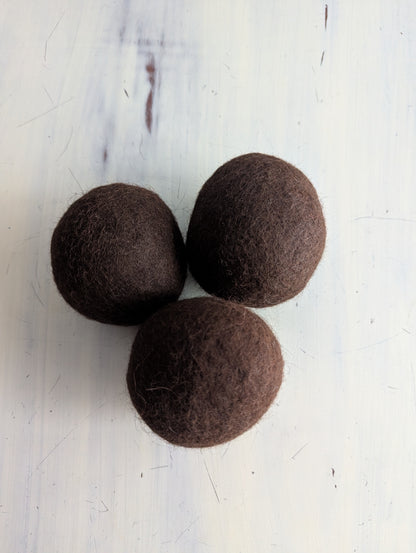 Three brown felt dryer balls on a white marble surface