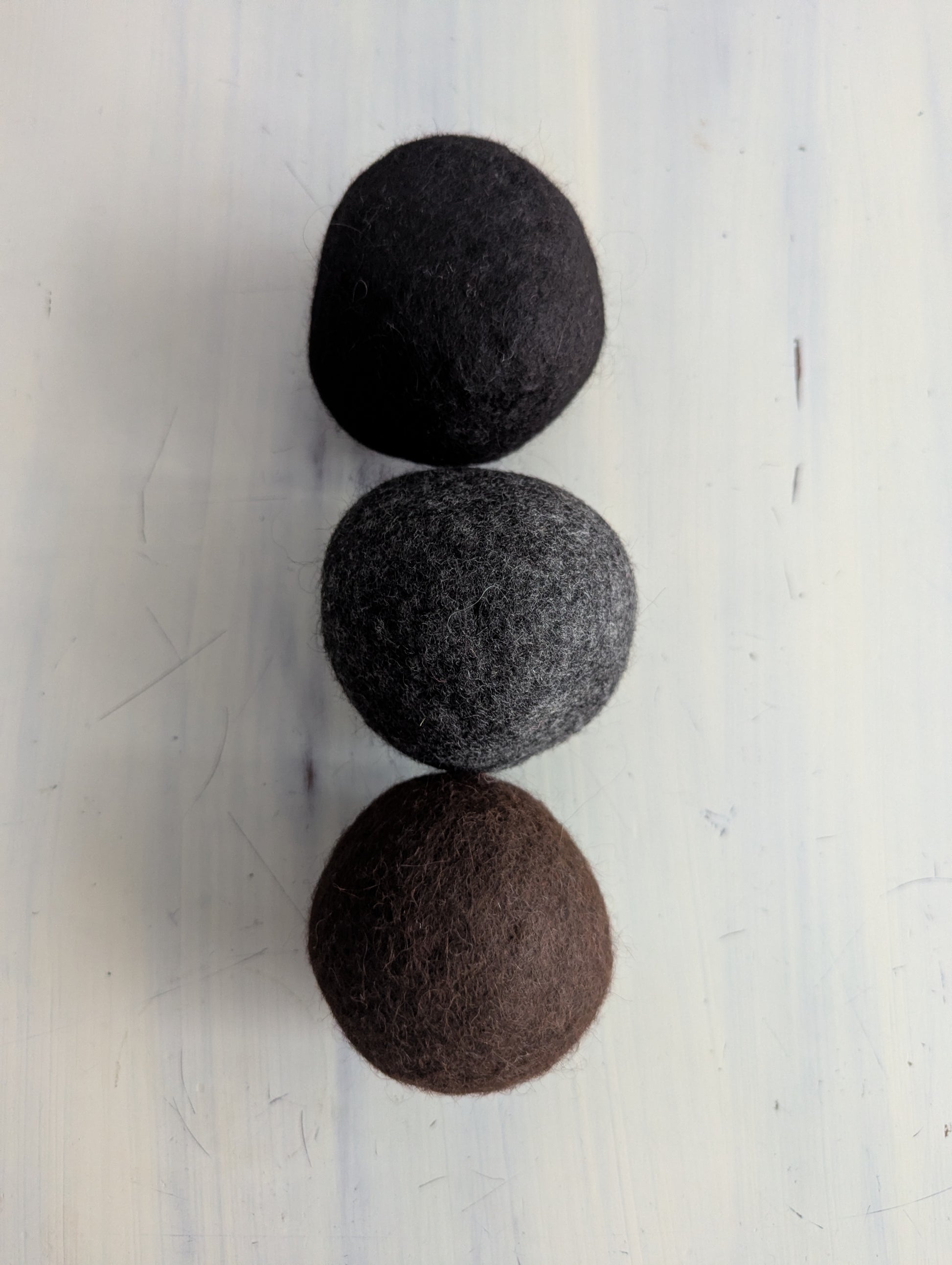 Three felted wool dryer balls in black, gray, and brown on a white background