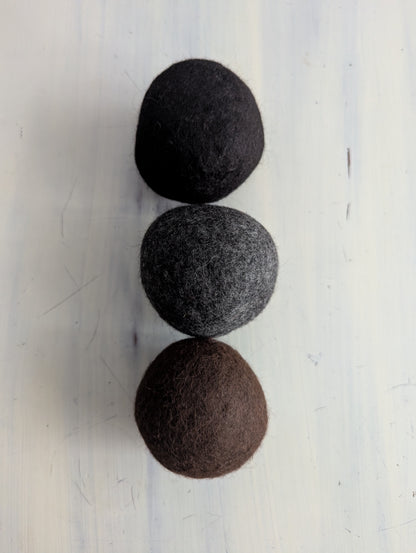 Three felted wool dryer balls in black, gray, and brown on a white background