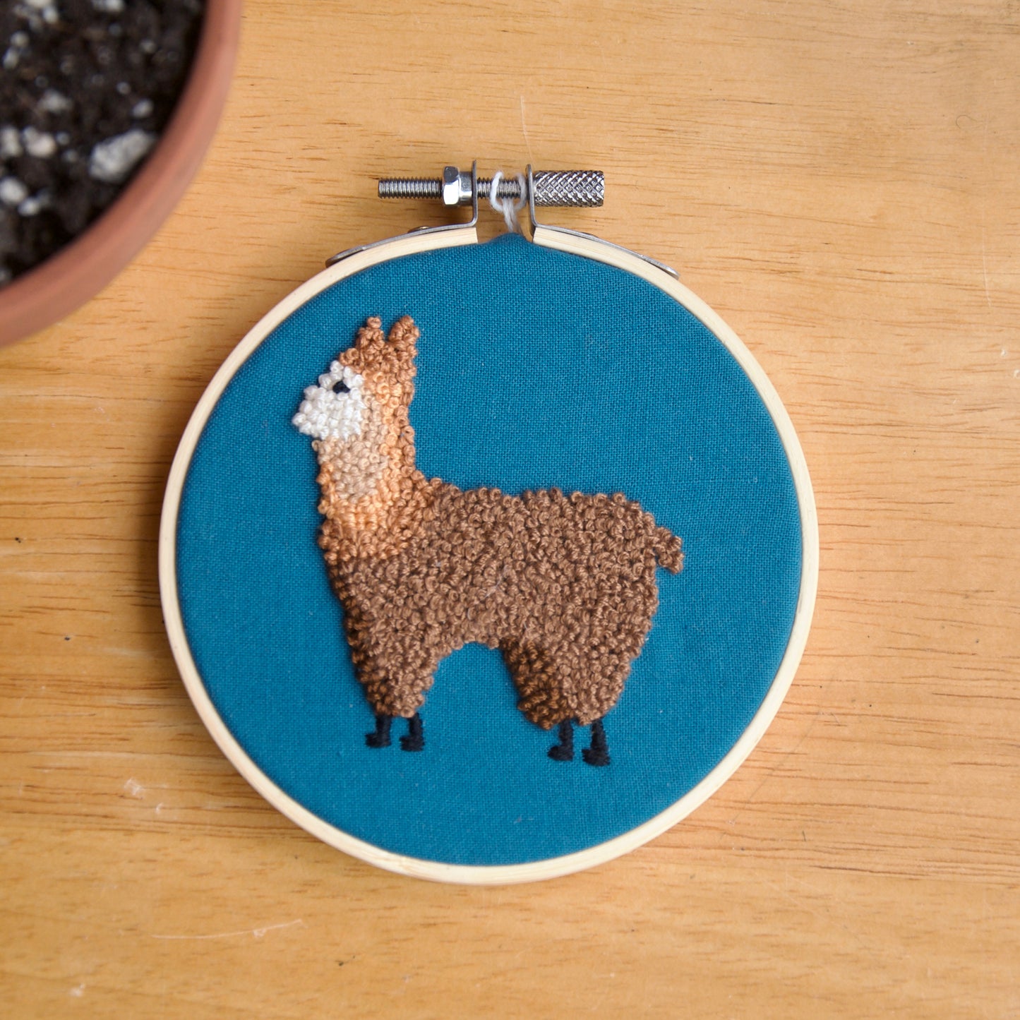 Hand stitched embroidery of an alpaca on a blue fabric background, mounted on a 4-inch wood hoop.