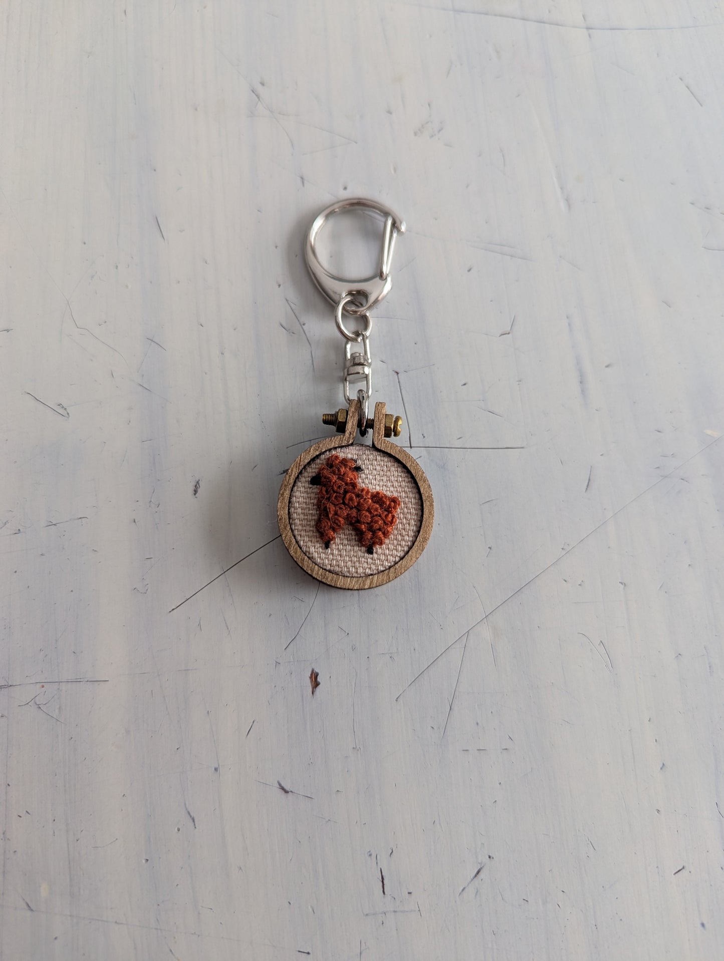 Keychain with an alpaca embroidered design on a textured white surface