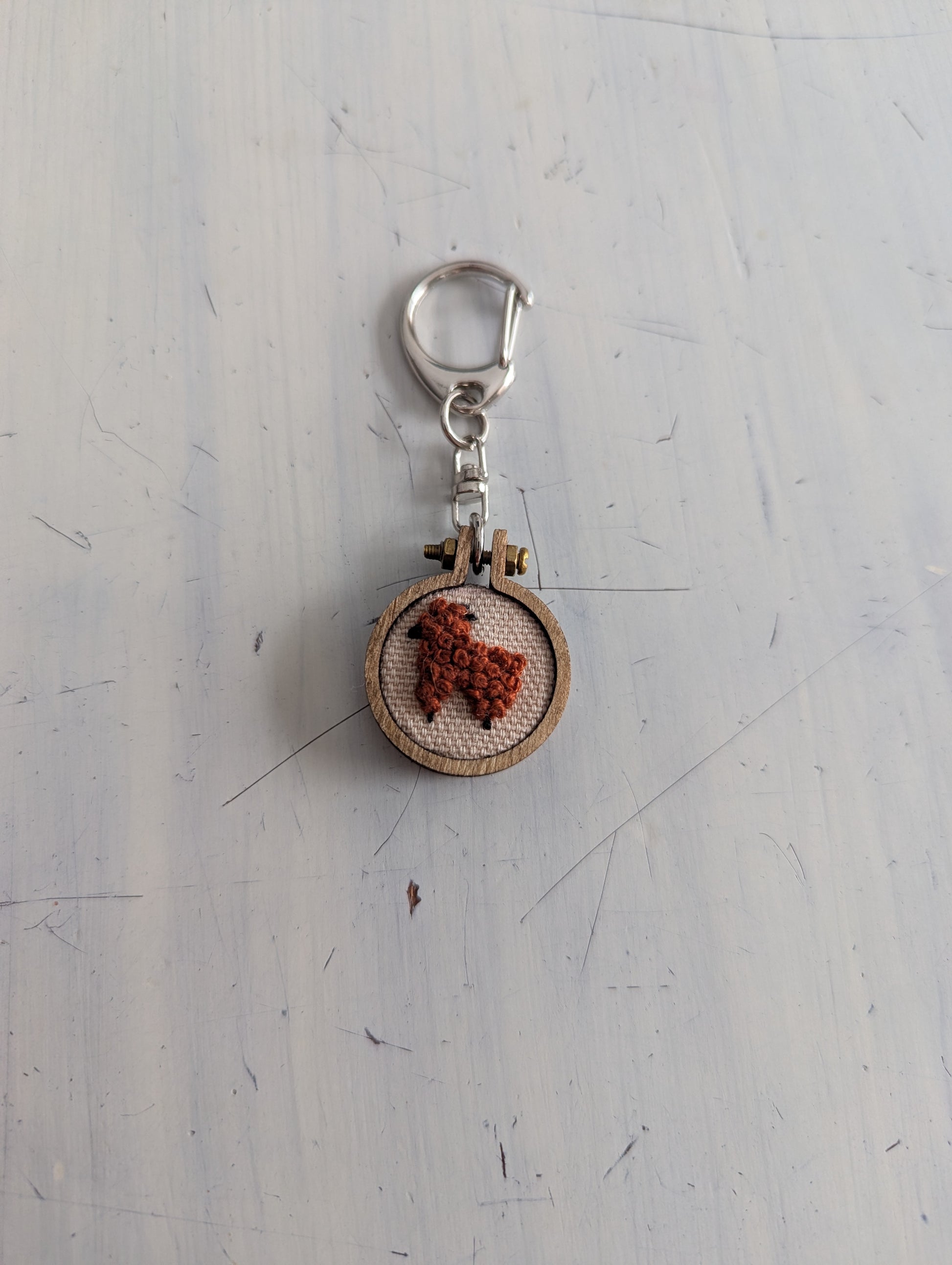 Keychain with an alpaca embroidered design on a textured white surface