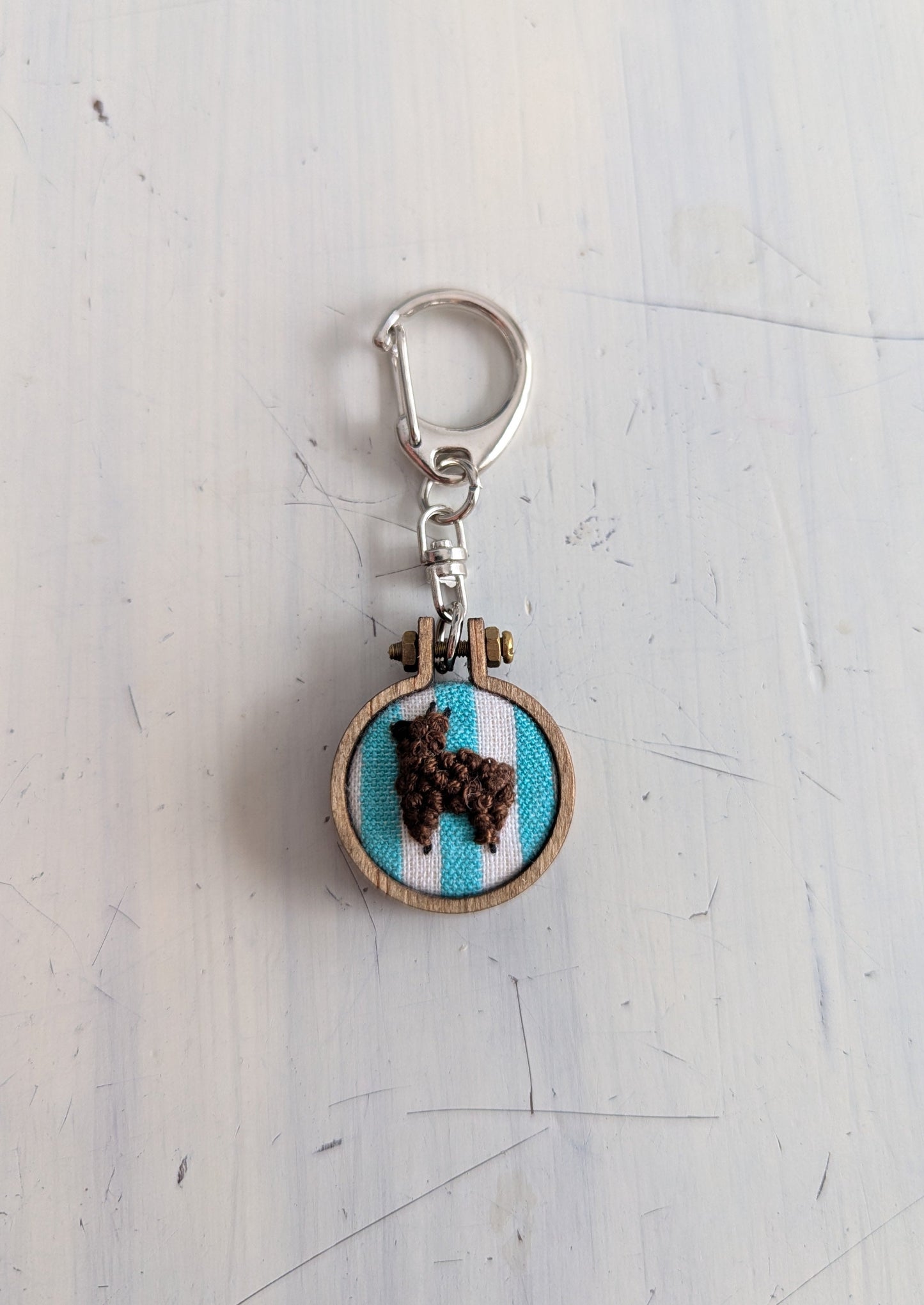 Keychain with embroidered design of an alpaca on a light blue background, attached to a metal clasp.