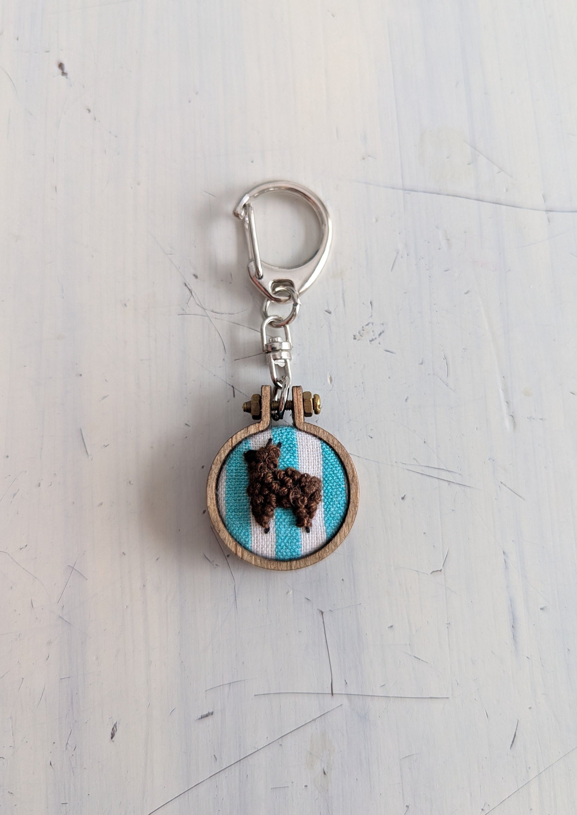 Keychain with embroidered design of an alpaca on a light blue background, attached to a metal clasp.