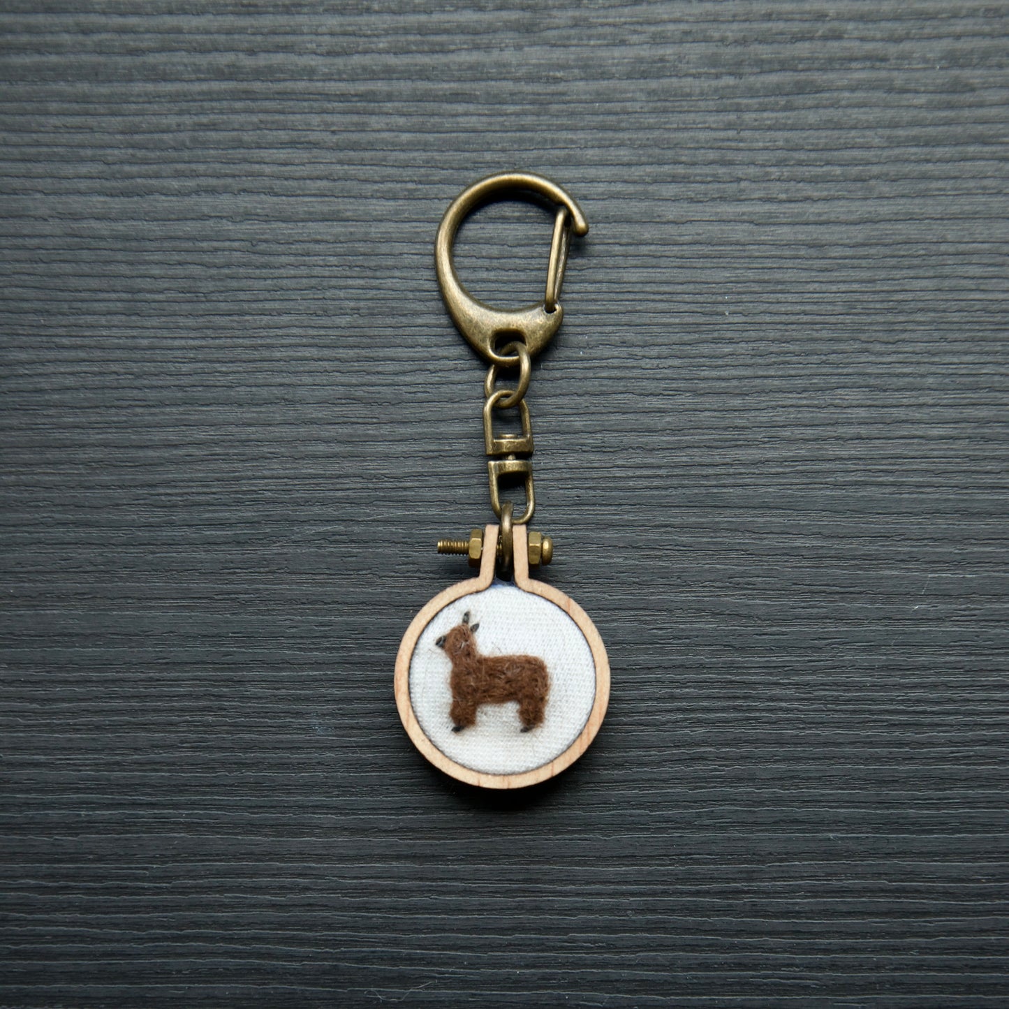 Needle felt alpaca on a small wooden keychain on a dark surface