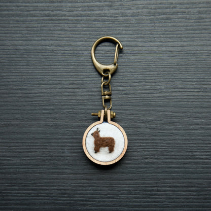 Needle felt alpaca on a small wooden keychain on a dark surface