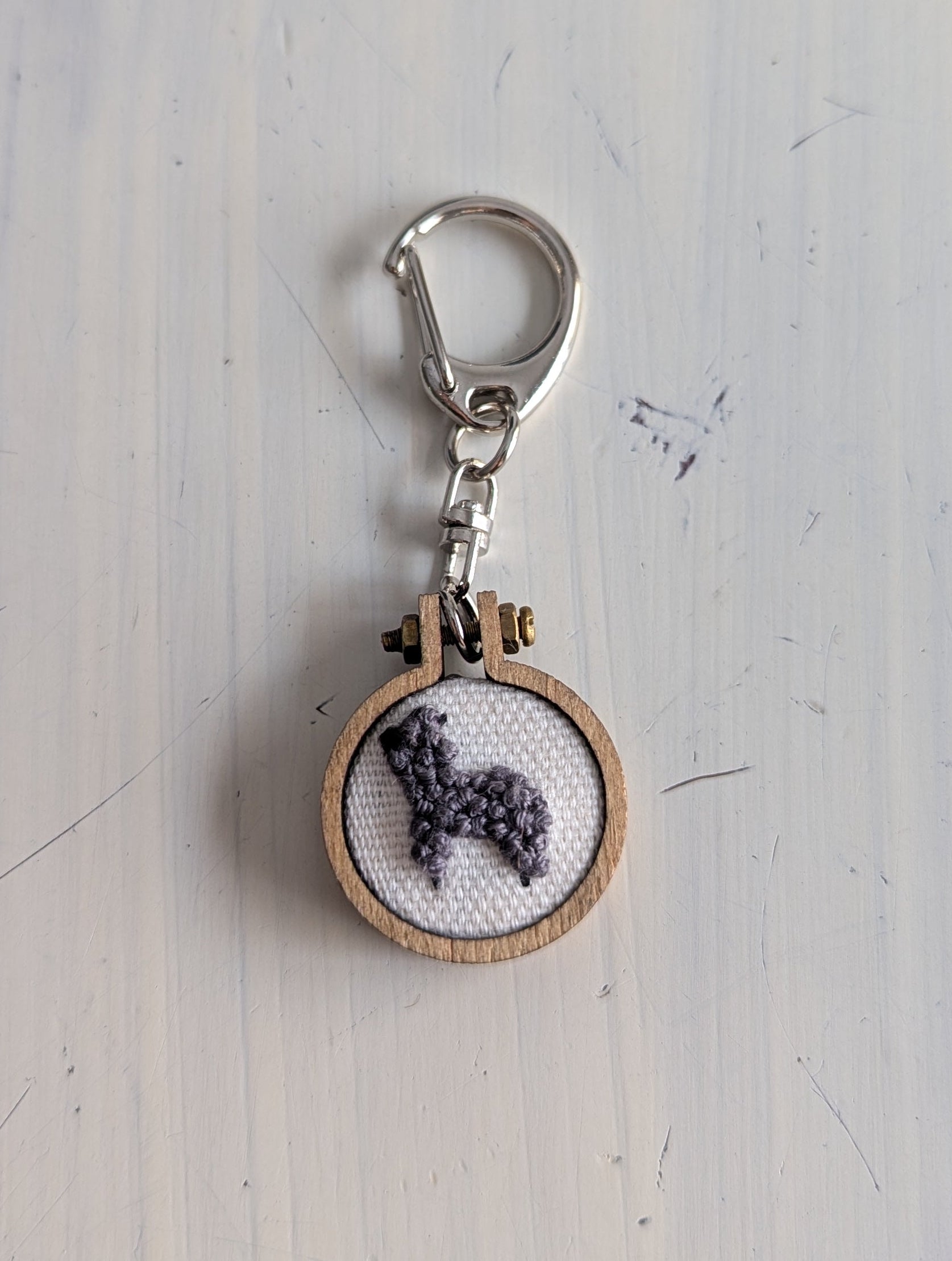 Keychain with alpaca cross-stitch design on a light wooden surface
