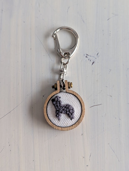 Keychain with alpaca cross-stitch design on a light wooden surface