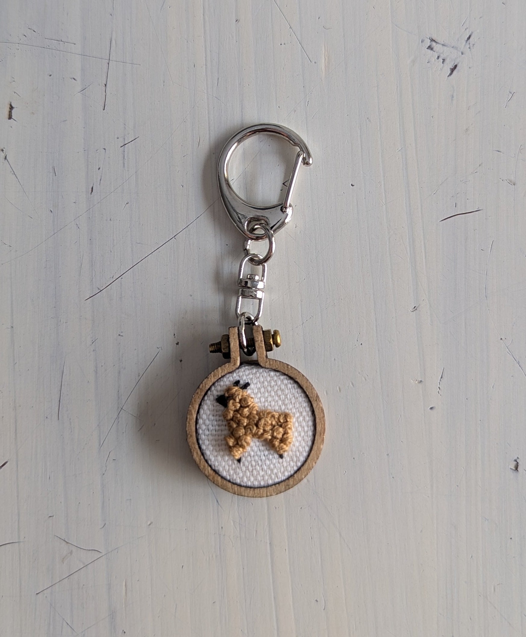 Round keychain with a small embroidered alpaca design on a light gray surface