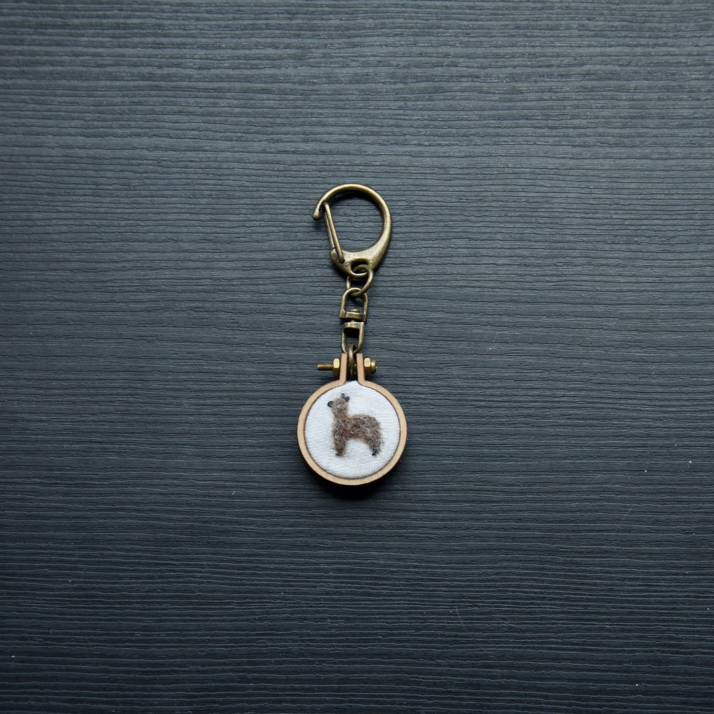 Needle felt alpaca on a small wooden keychain on a dark surface