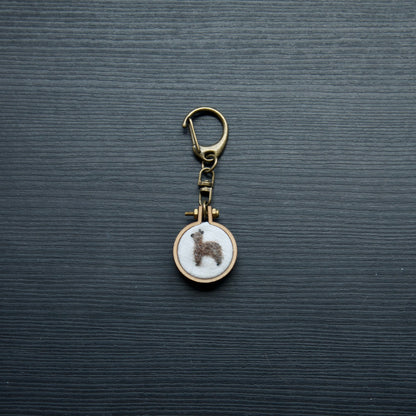 Needle felt alpaca on a small wooden keychain on a dark surface