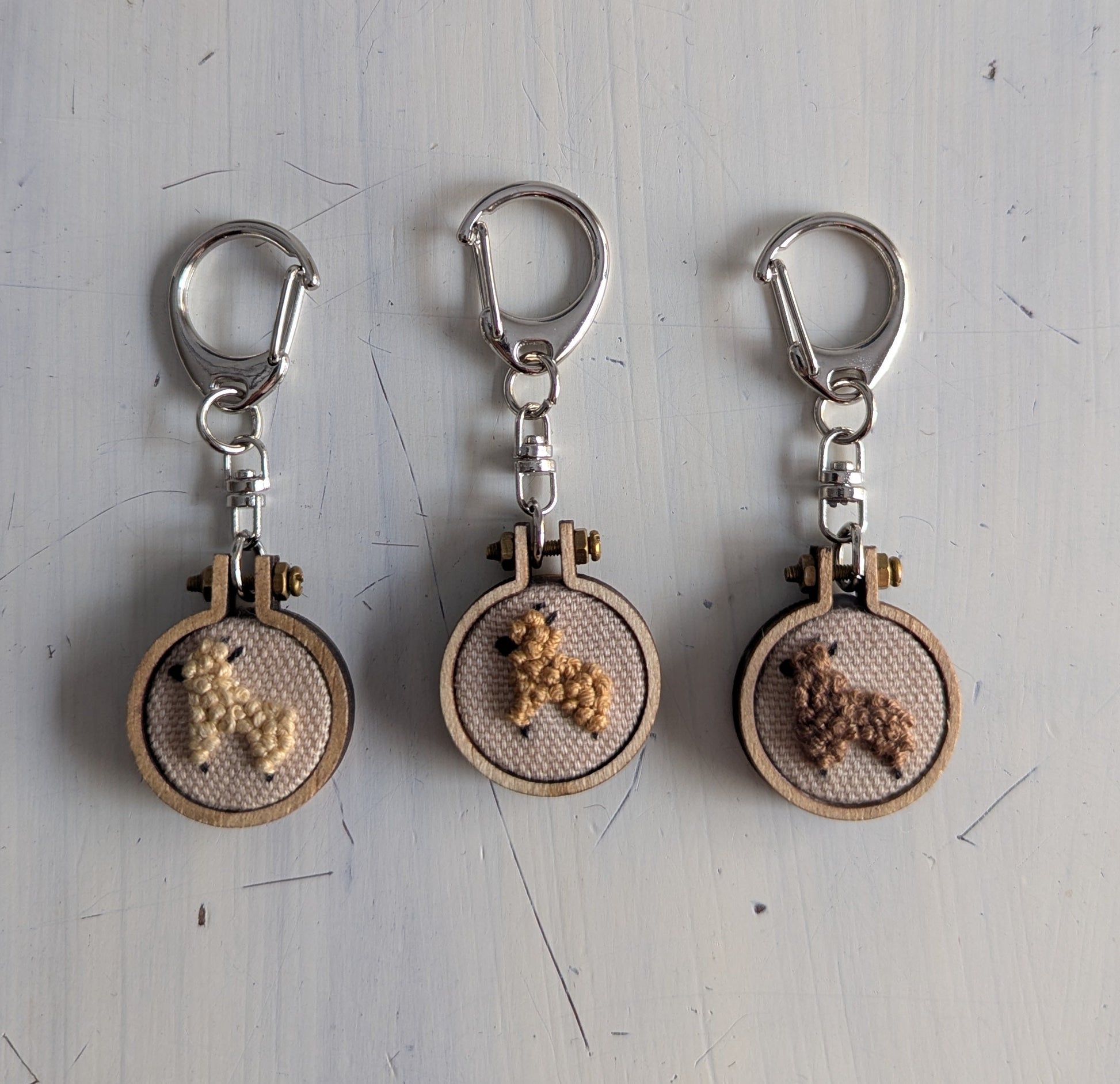 Three embroidered keychains with alpaca designs on a light gray surface