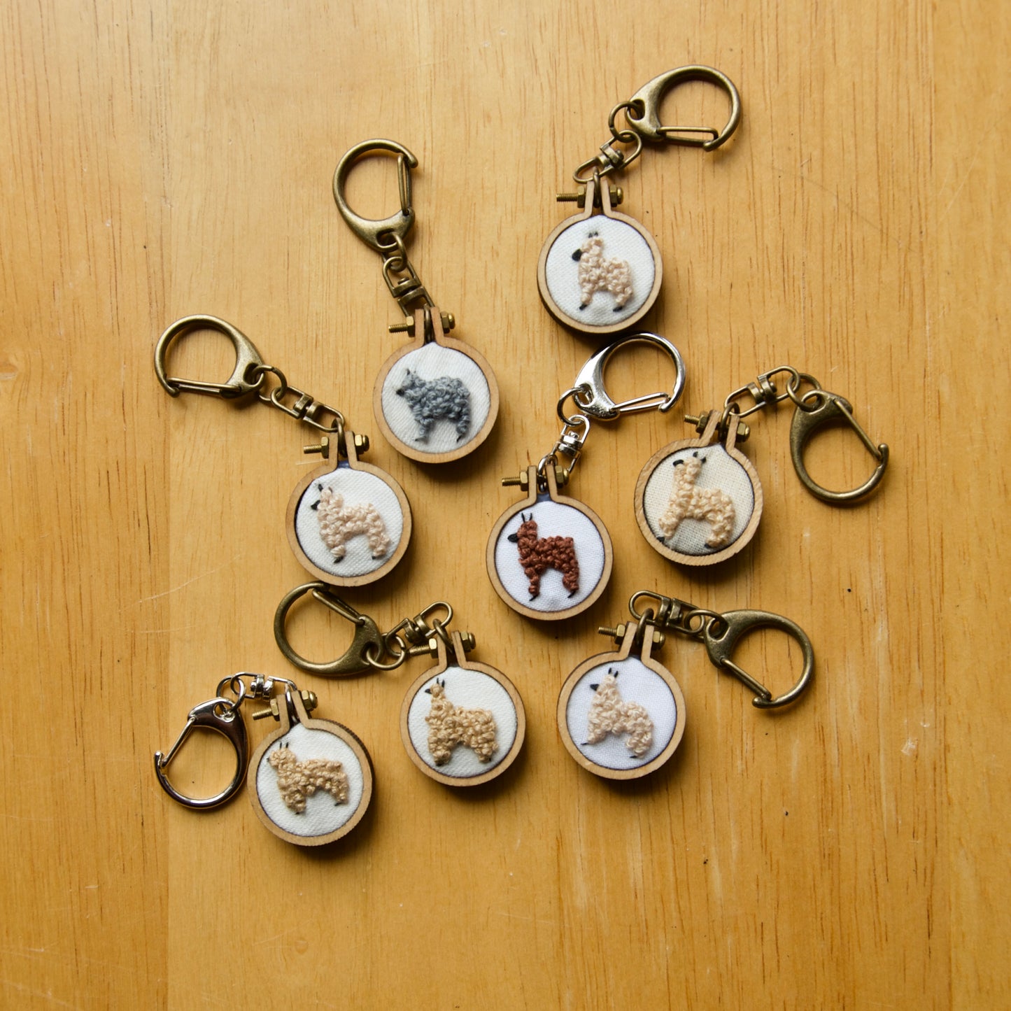 Embroidery alpaca on a fabric circle, inside a small wooden keychain on a wood surface