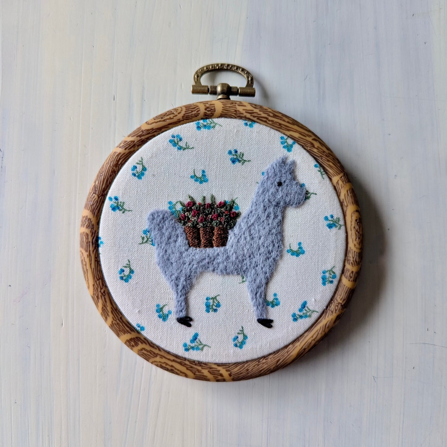 Embroidery hoop with a llama wearing a flower basket of flowers on a white background