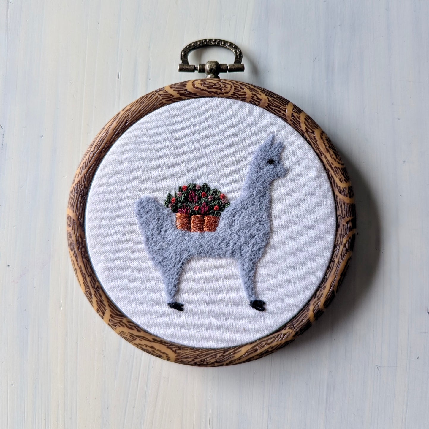 Embroidery hoop with a llama wearing a basket of flowers on a white background