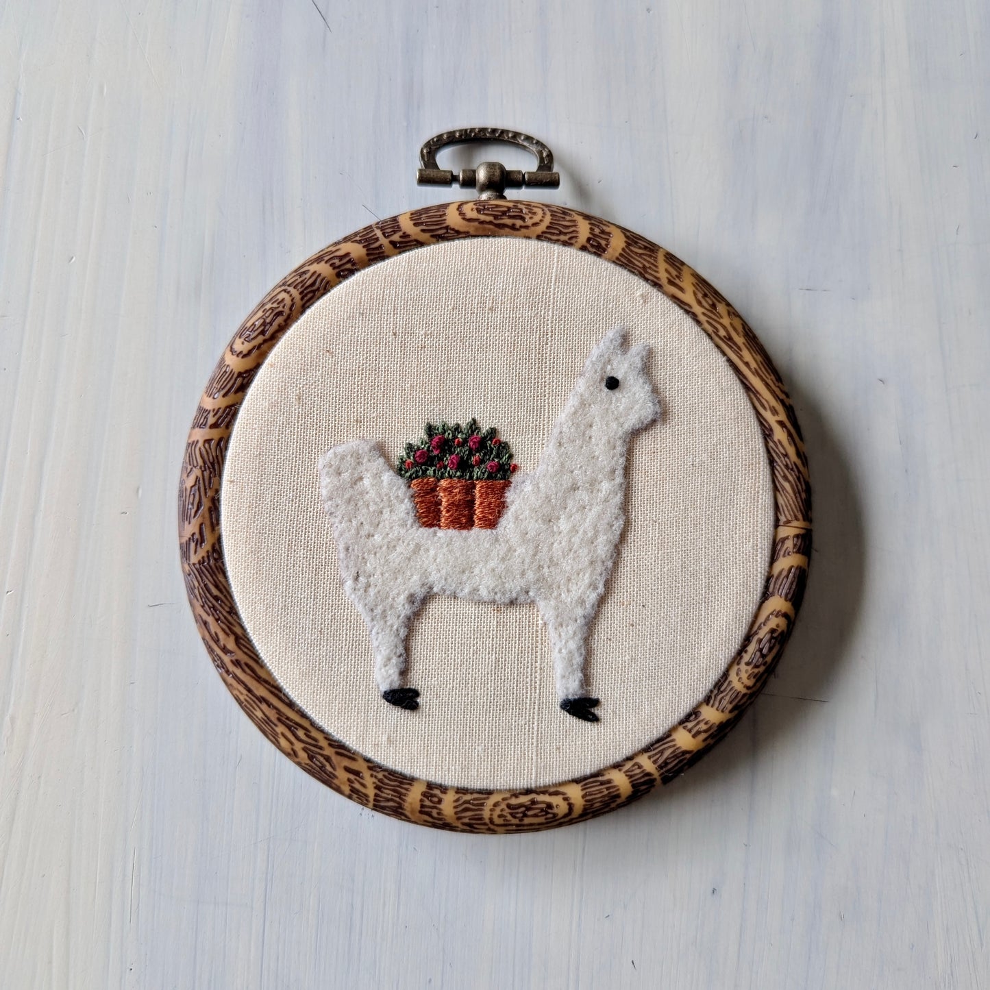 White alpaca needle felt art in a wooden hoop on a light wooden surface