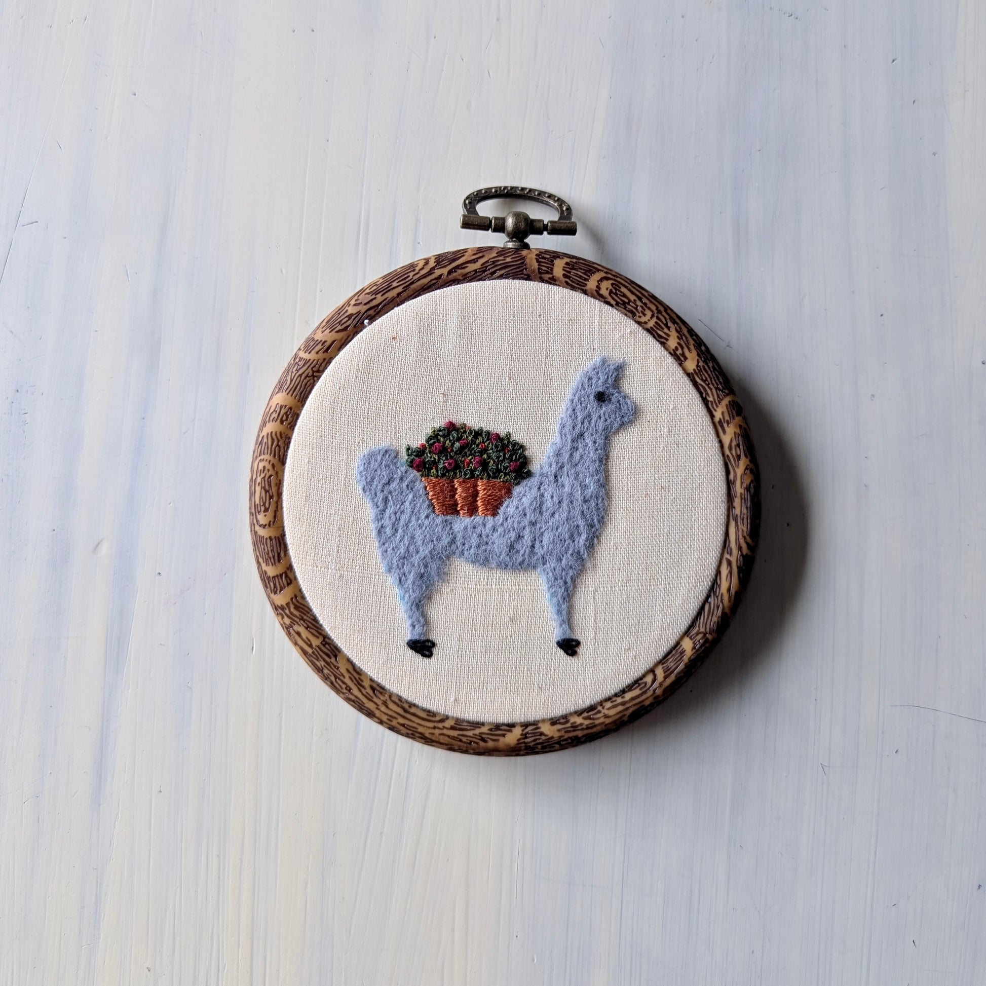 Embroidery hoop with a llama design on a light wooden surface