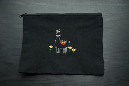 A black zip pouch with an embroidery alpaca in a flower field on a dark surface