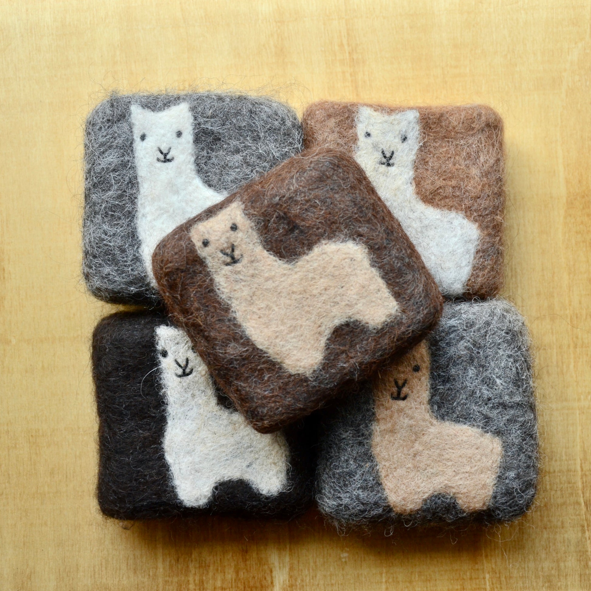 A small collection of square felted soap bars on a wooden surface
