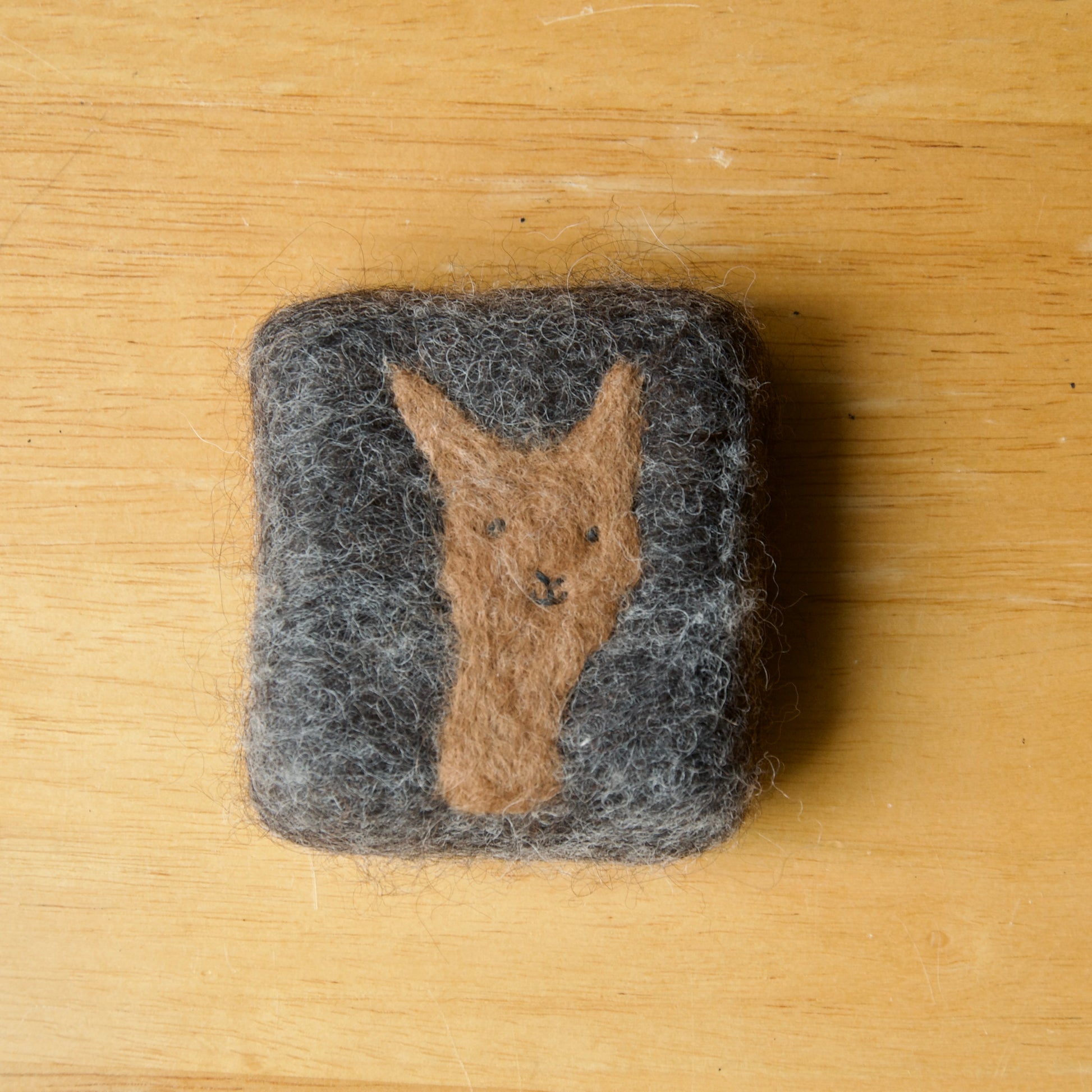 A square felted soap bar on a wooden surface