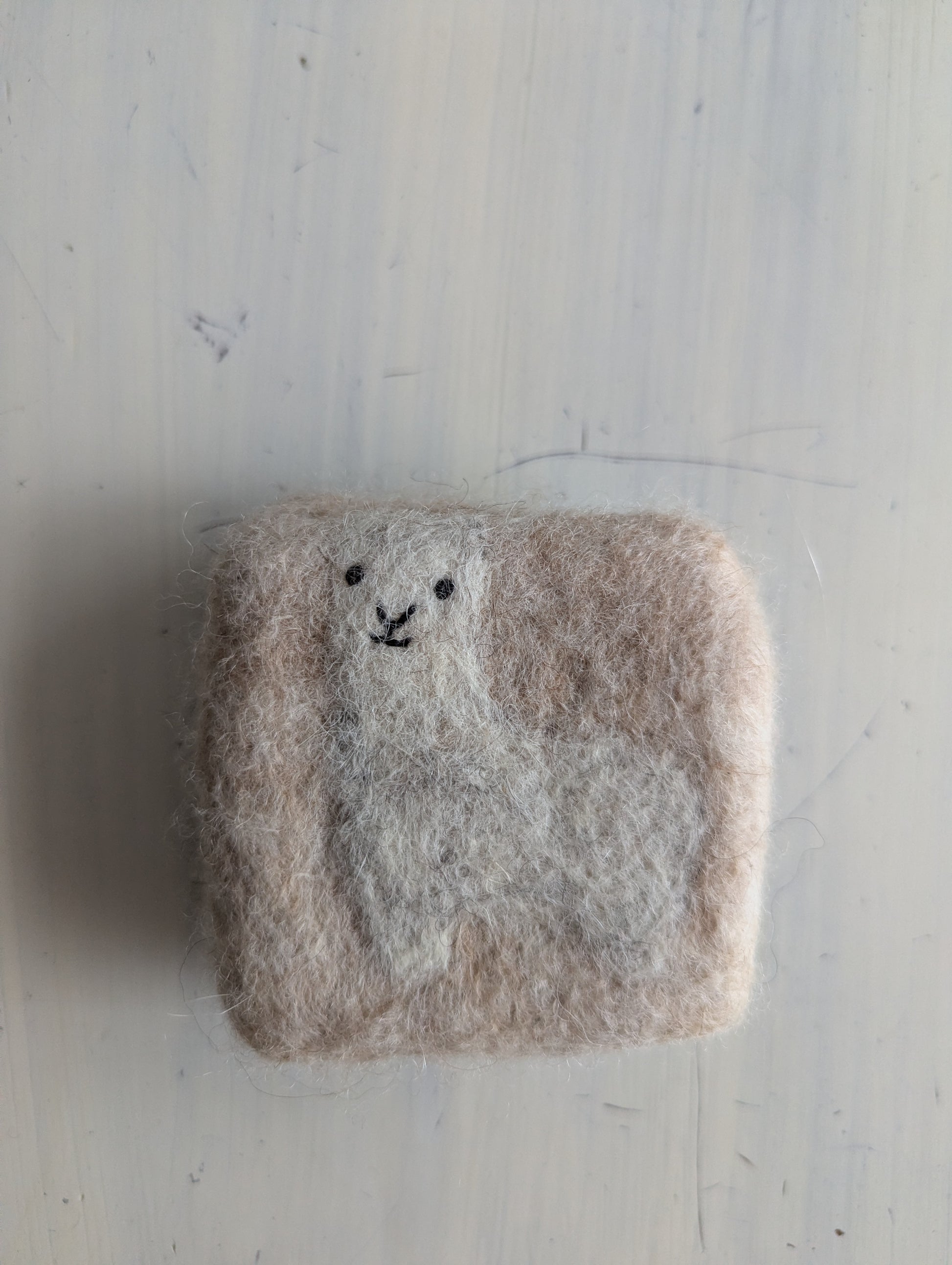 Felted soap with a white alpaca body and face on a cream background