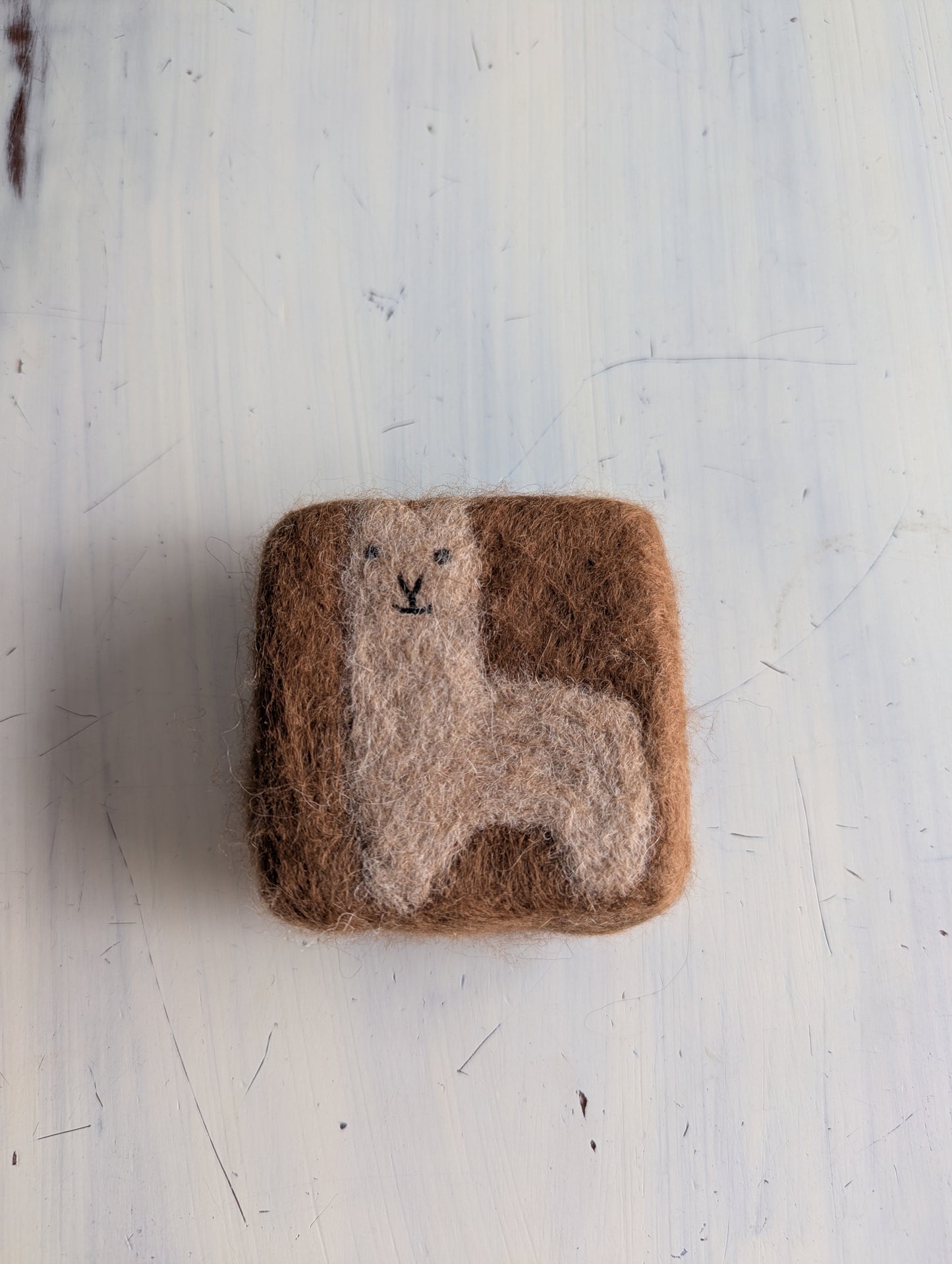 Square felted product with a llama design on a light gray background