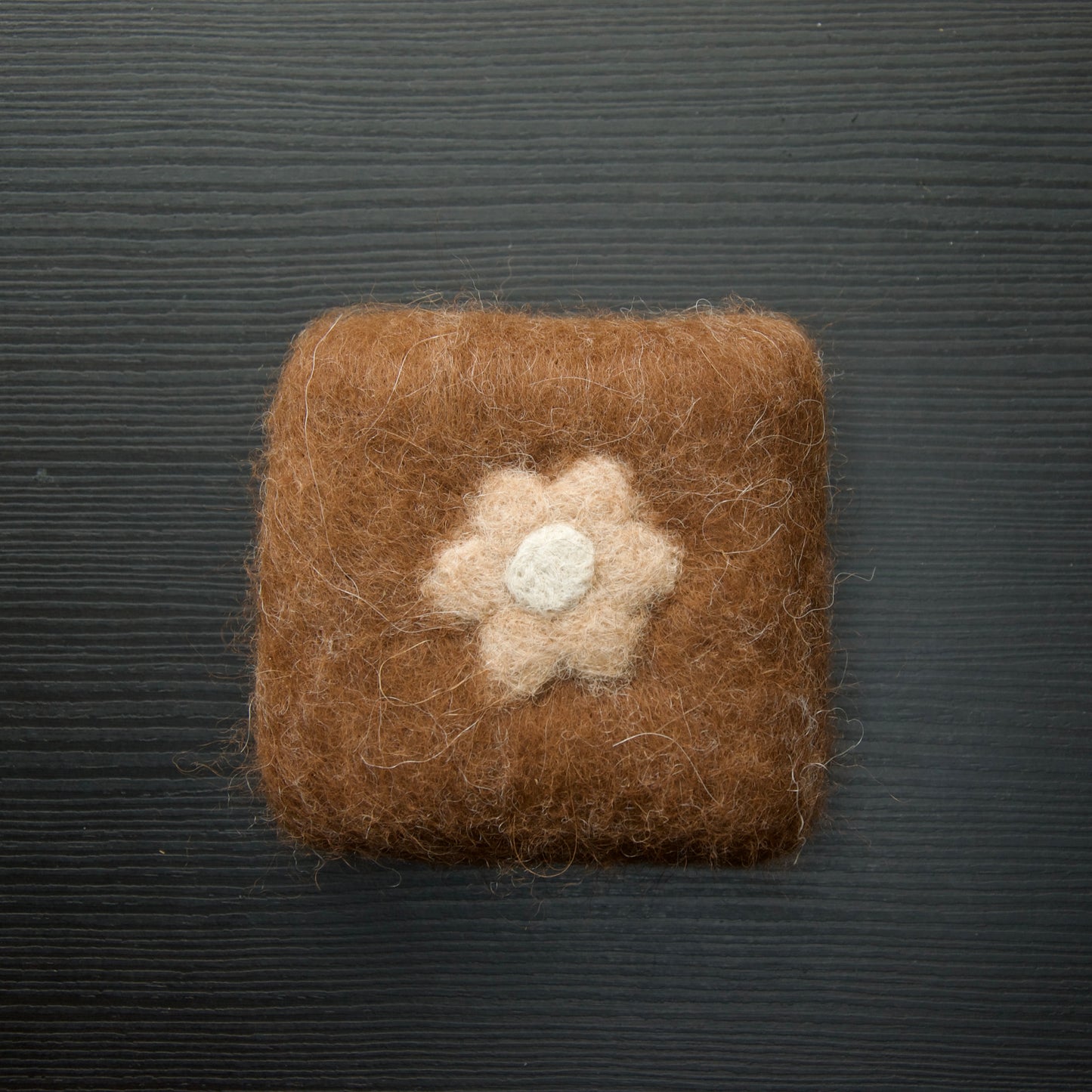 A felted soap bar with a flower design on a dark background.