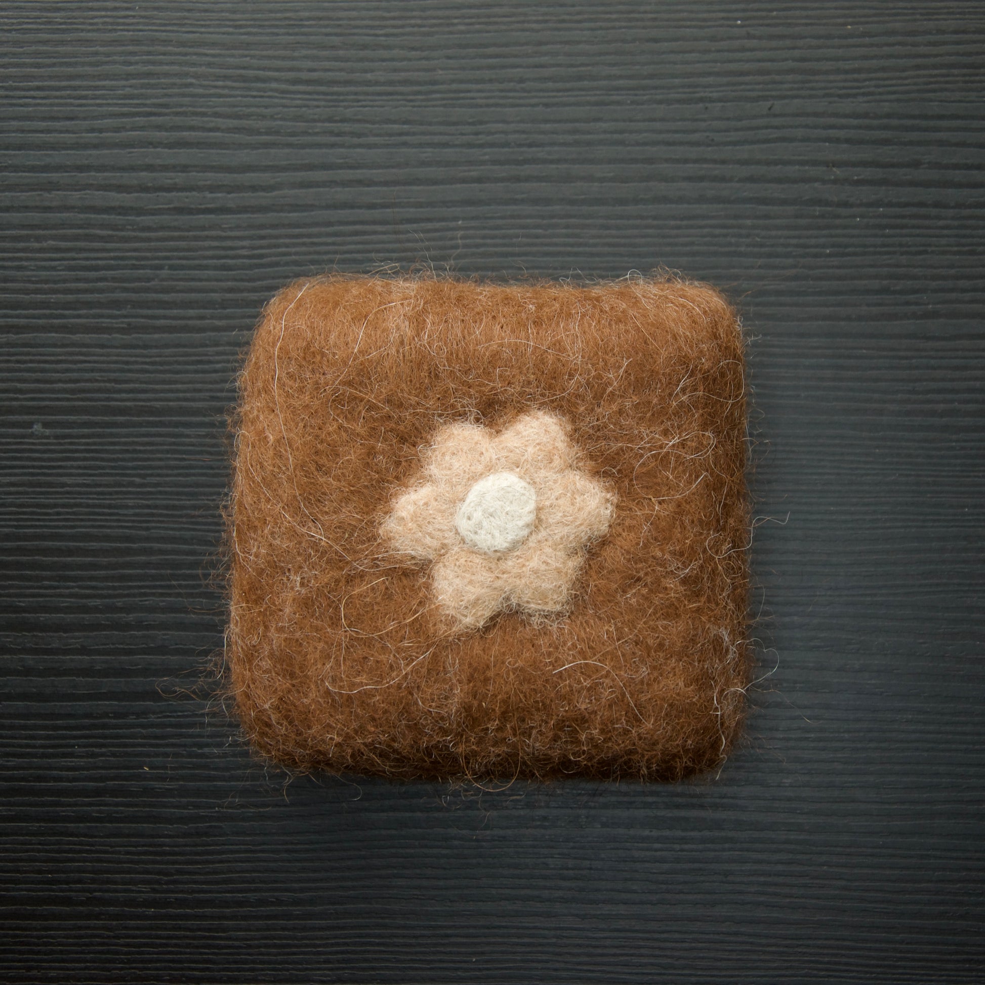 A felted soap bar with a flower design on a dark background.