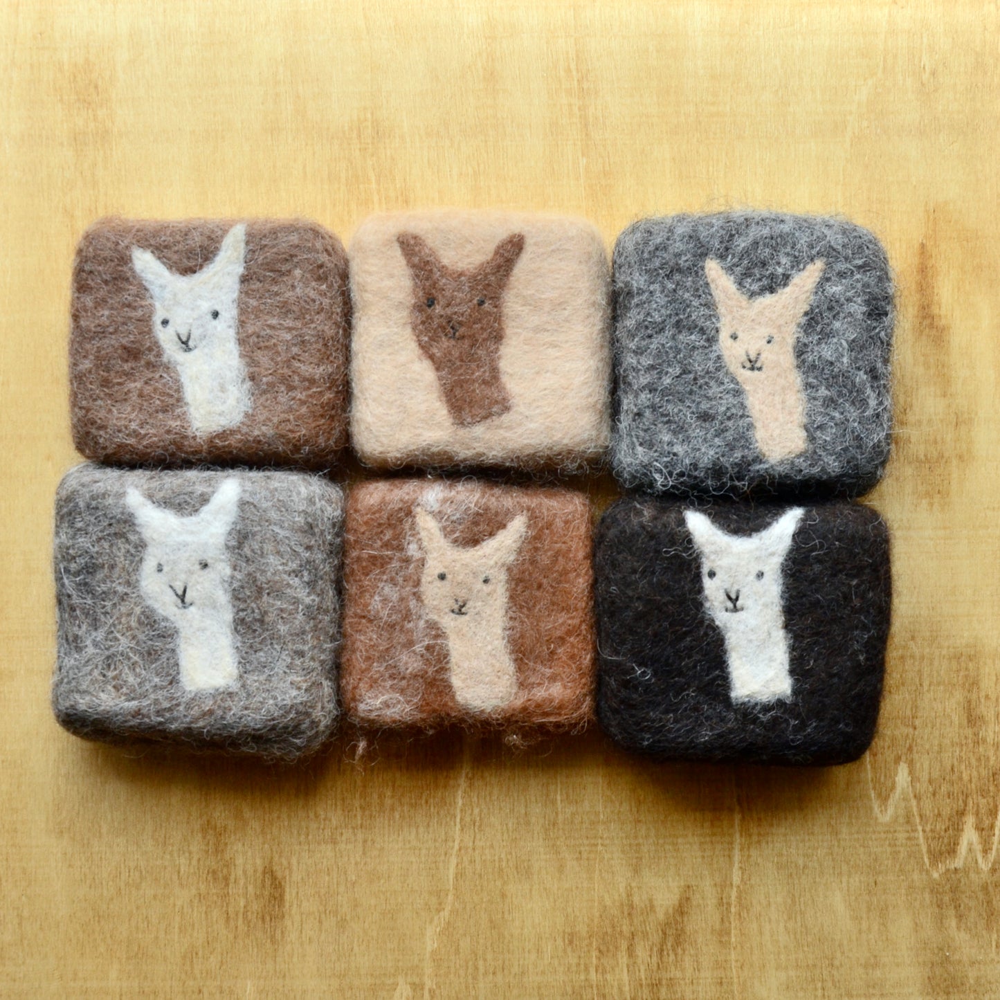 A collection of square felted soap bars on a wooden surface