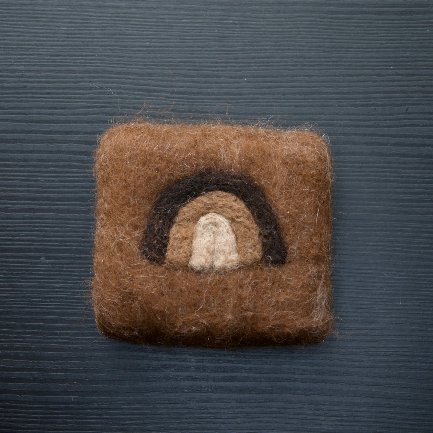 A felted soap bar with a rainbow design on a dark background.