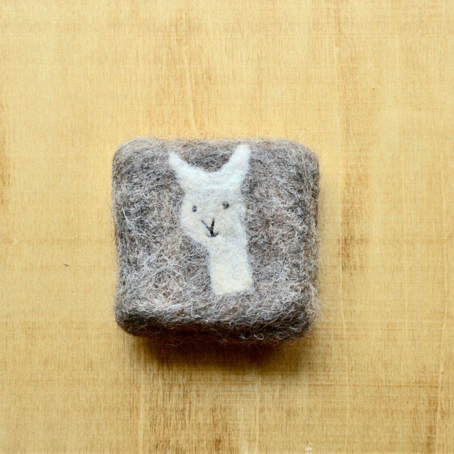 A square felted soap bar on a wooden surface