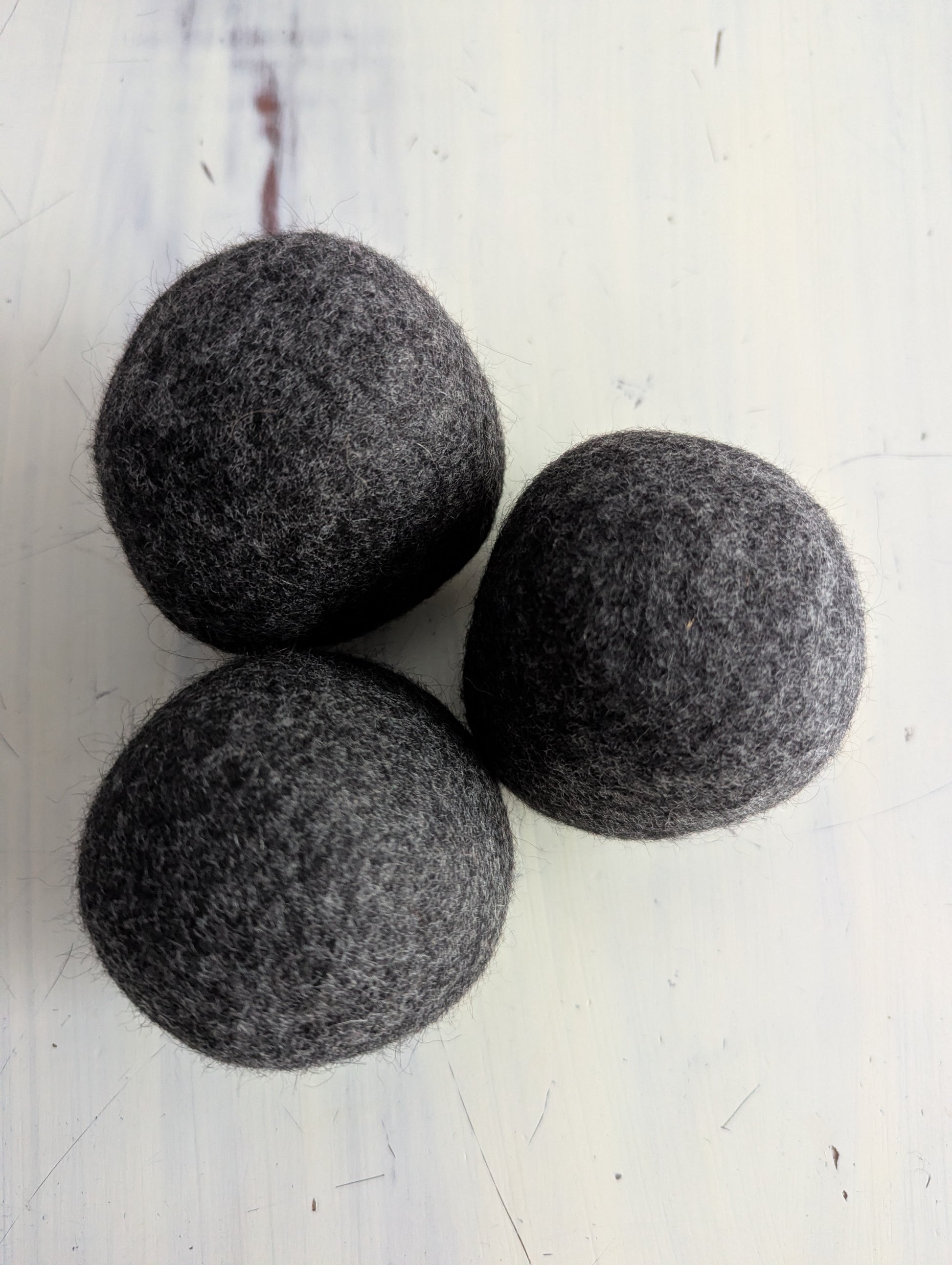 Three gray felt dryer balls on a white surface