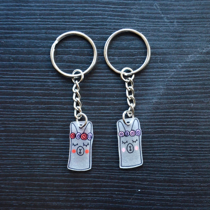 A collection of hand-drawn keychains with various cute designs, attached to silver split loops with chains. The keychains are made from recycled plastic and are in different colors, featuring simple, minimalistic alpaca designs.