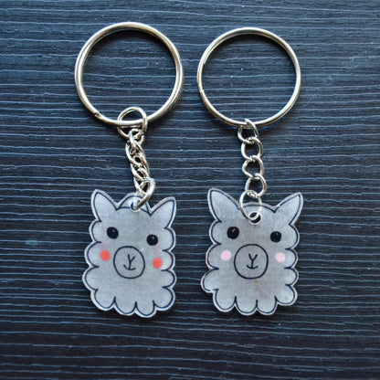 A collection of hand-drawn keychains with various cute designs, attached to silver split loops with chains. The keychains are made from recycled plastic and are in different colors, featuring simple, minimalistic alpaca designs.
