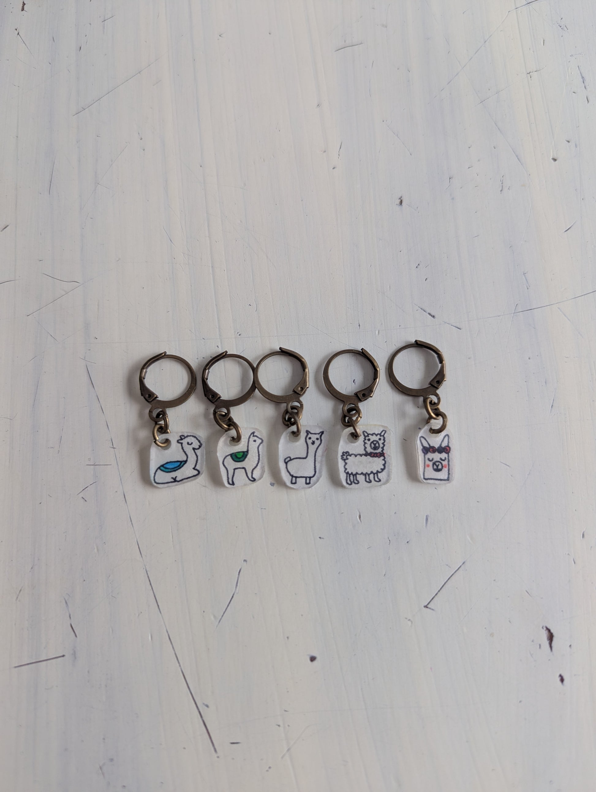 Five keychains with alpaca illustrations on a white surface