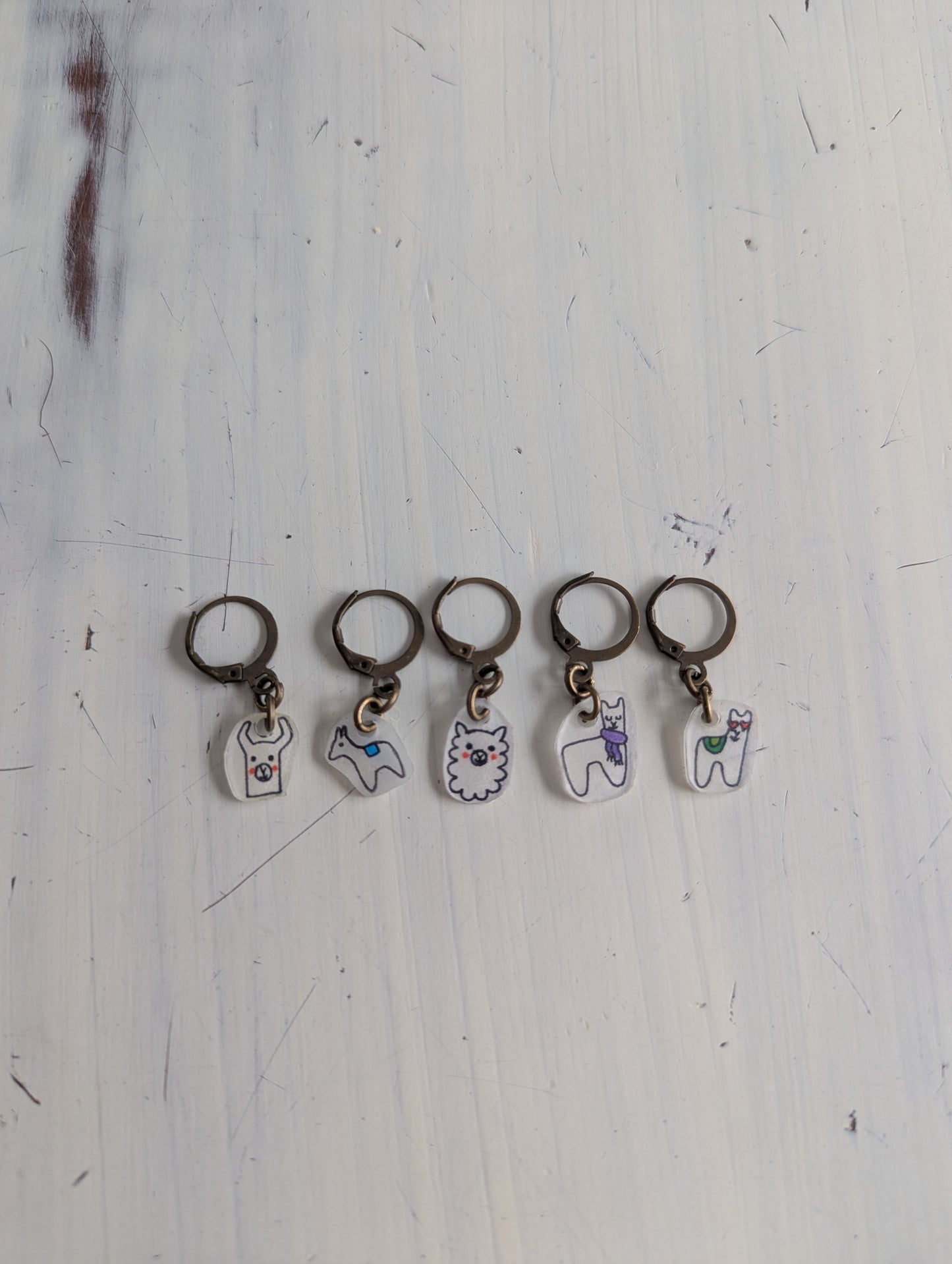 Set of five keychains with different alpaca designs on a light wooden surface.