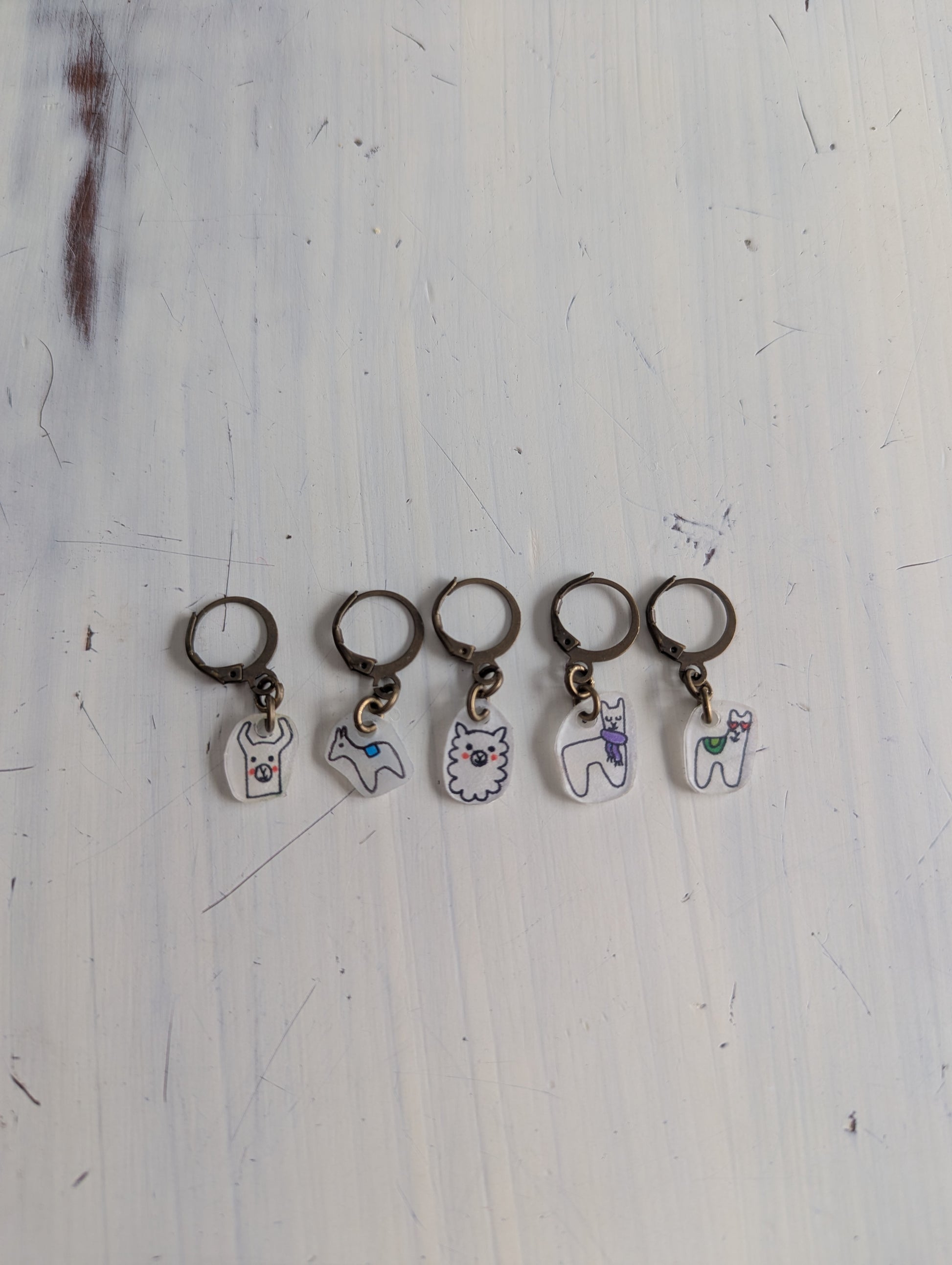 Set of five keychains with different alpaca designs on a light wooden surface.
