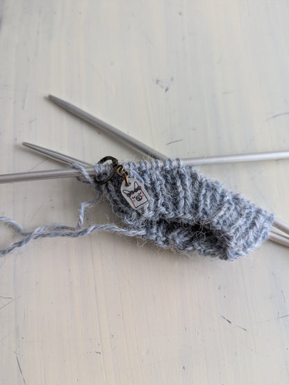 Knitted gray yarn with knitting needles on a light wooden surface, using a hand made needle minder