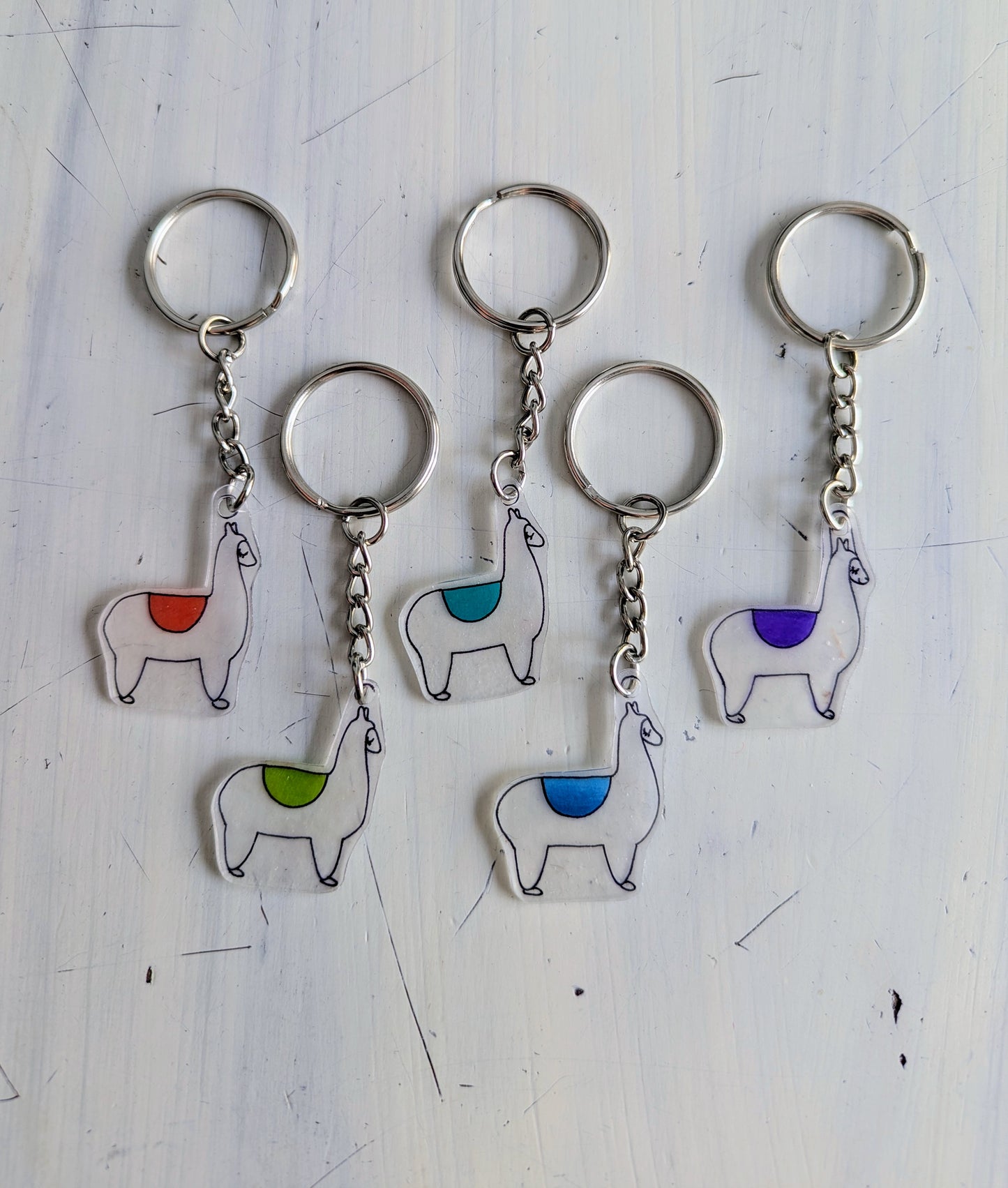 Set of five llama-shaped keychains with colorful pads on a white background