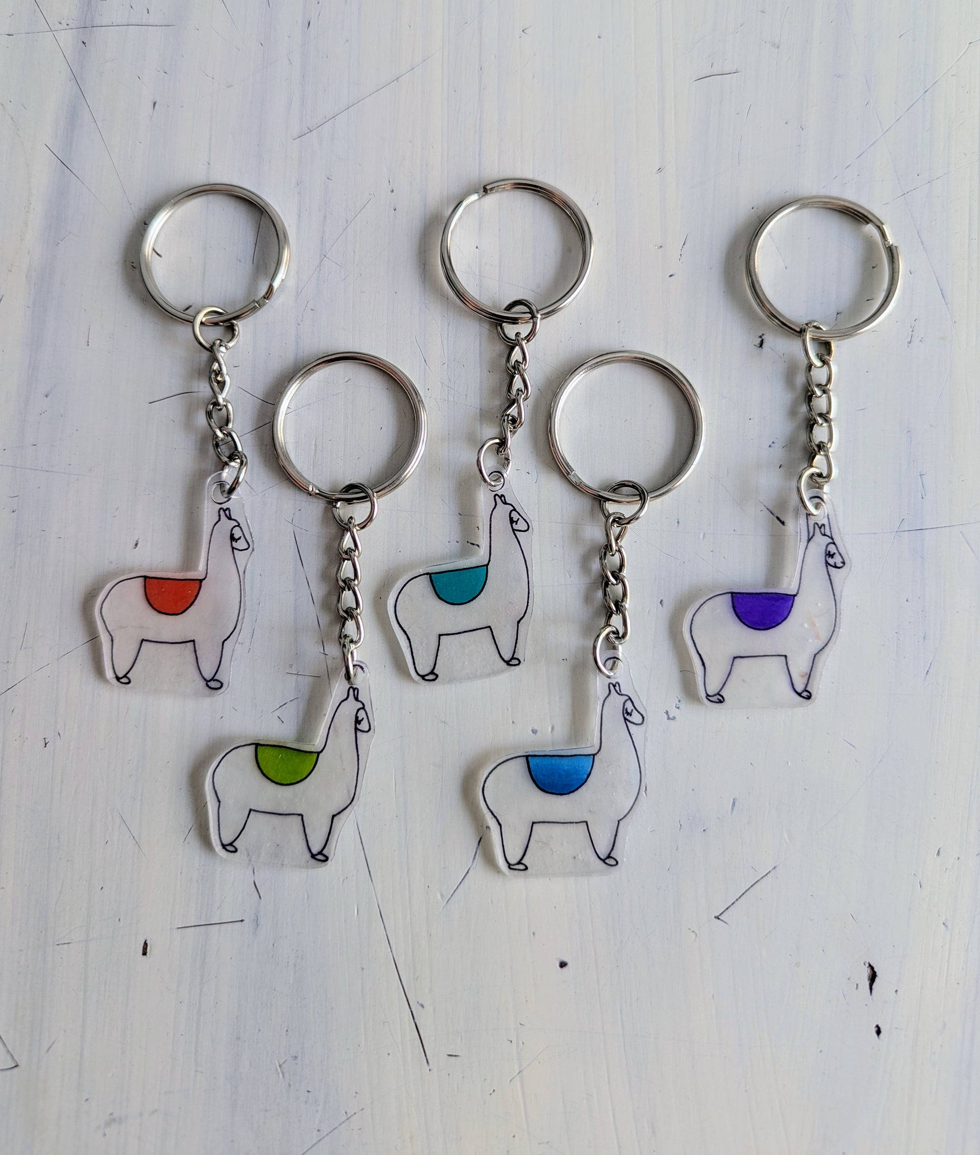 Set of five llama-shaped keychains with colorful pads on a white background
