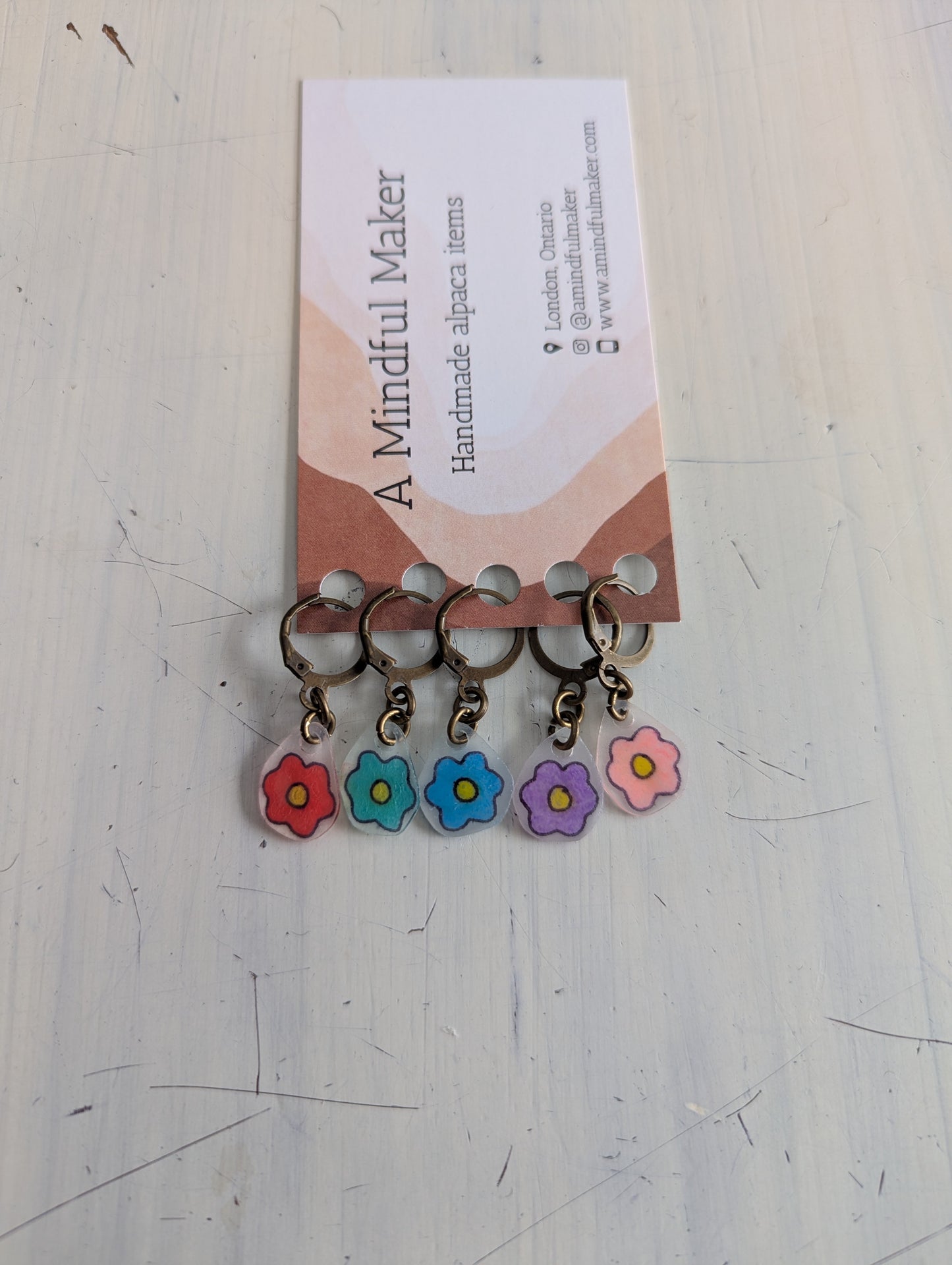 Set of colorful hand drawn flower-shaped keychain charms on a white surface with a card labeled 'A Mindful Maker'.