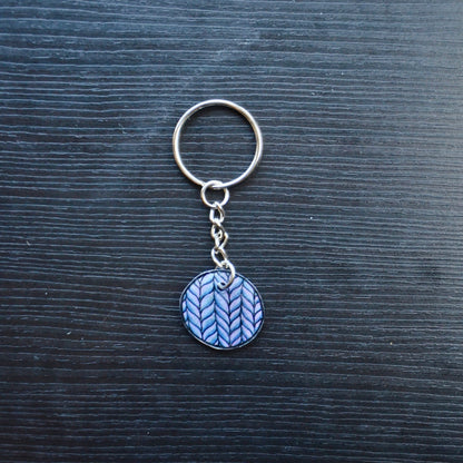 A set of colorful hand-drawn keychains made from recycled plastic, displayed on a dark wooden surface. Each keychain has a silver split loop and chain attachment.