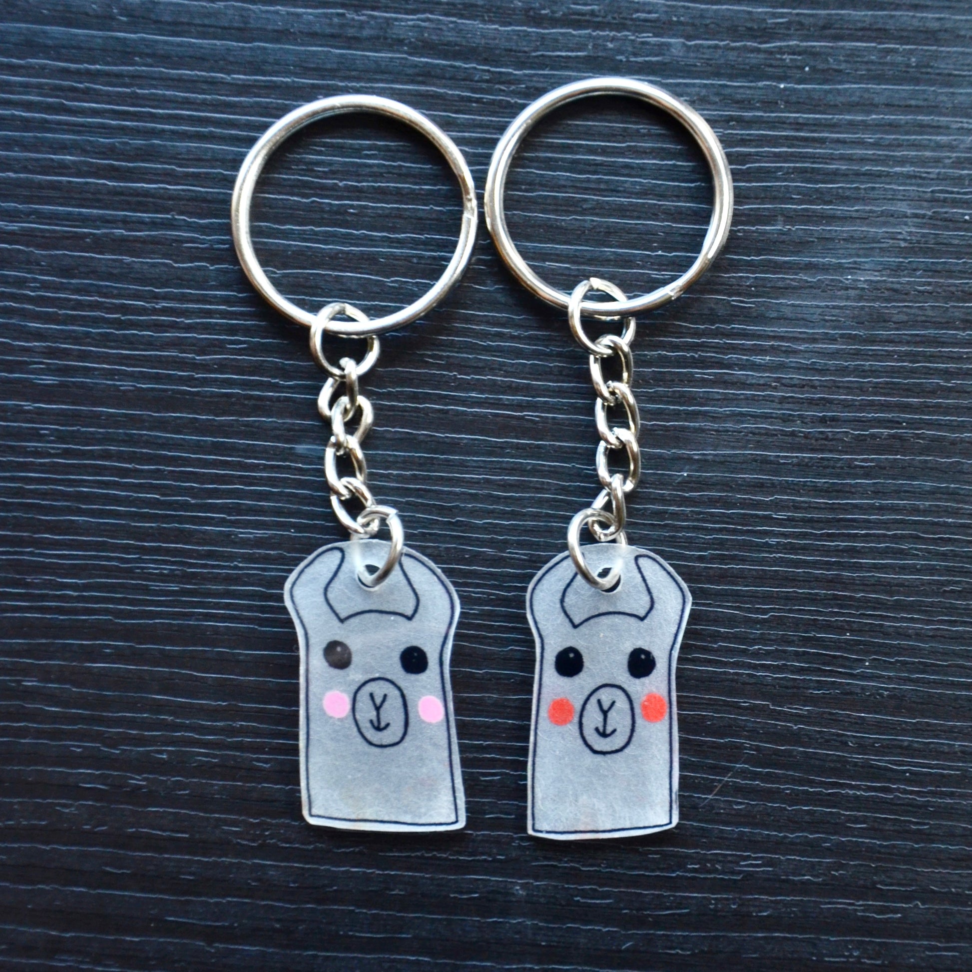 A collection of hand-drawn keychains with various cute designs, attached to silver split loops with chains. The keychains are made from recycled plastic and are in different colors, featuring simple, minimalistic alpaca designs.