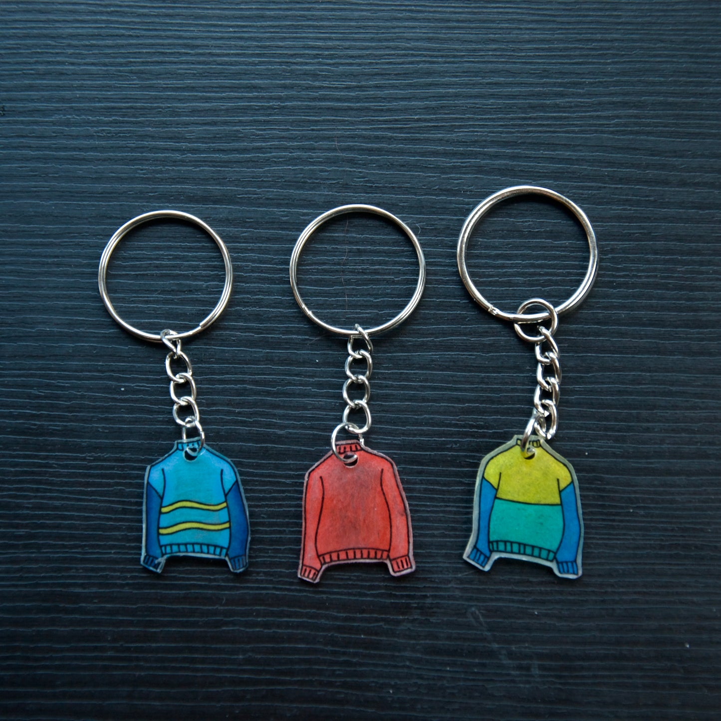 A collection of colorful hand-stitched keychains made from recycled plastic, displayed on a dark surface.