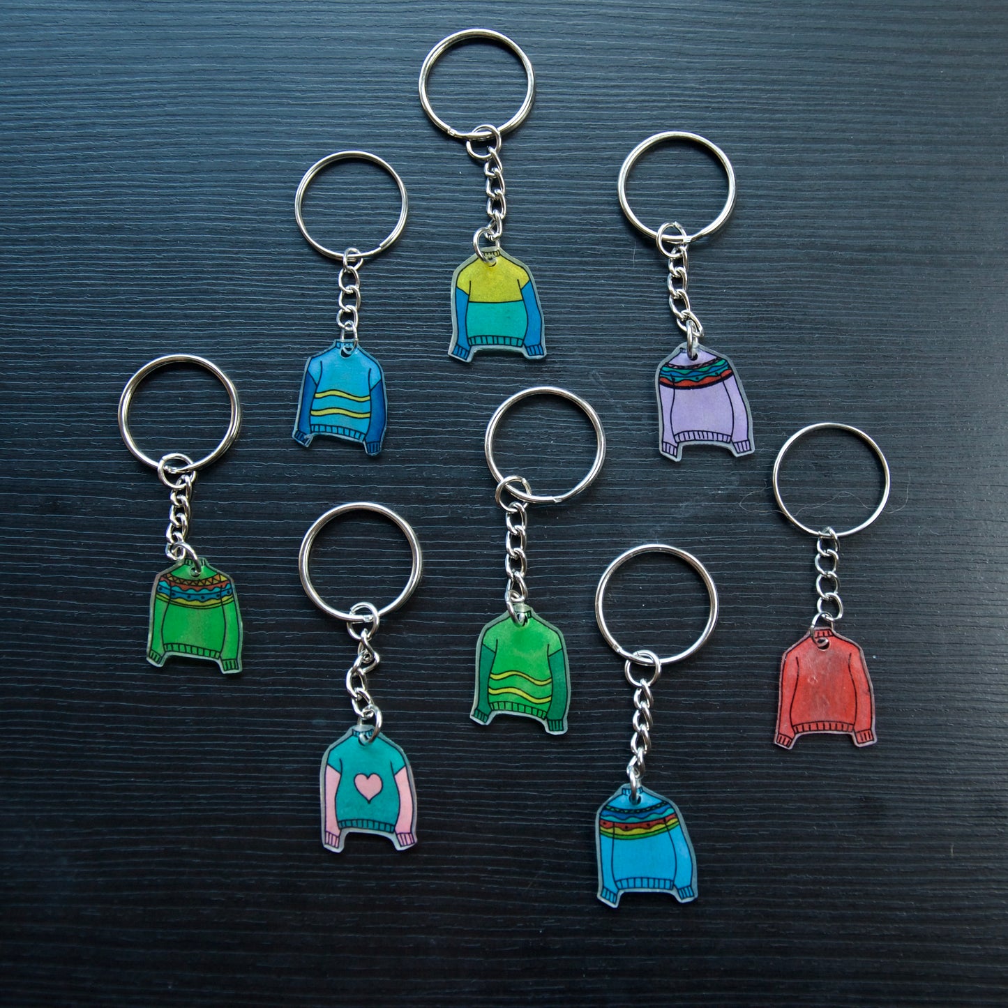 A collection of colorful hand-stitched keychains made from recycled plastic, displayed on a dark surface.